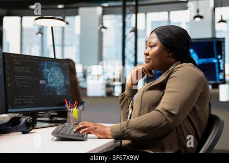 Joyful IT employee in tech startup uses AI on PC to optimize performance and forecast issues. Happy software developer in office training machine learning models using computer Stock Photo