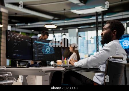 IT specialist in wheelchair using AI automation, refining algorithms for faster processing. Programmer with paraplegia in inclusive office using artificial intelligence for resource optimization Stock Photo