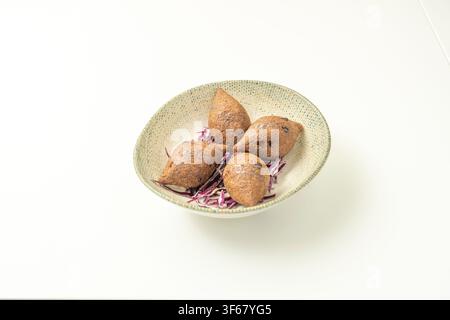 Four fried kibbeh shells arranged on shredded purple cabbage in speckled ceramic bowl Stock Photo