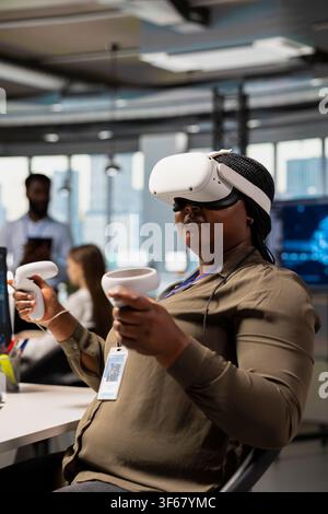 Software developer wearing VR goggles at office desk developing programs using AI automation. African american IT expert using virtual reality, debugging applications with artificial intelligence Stock Photo