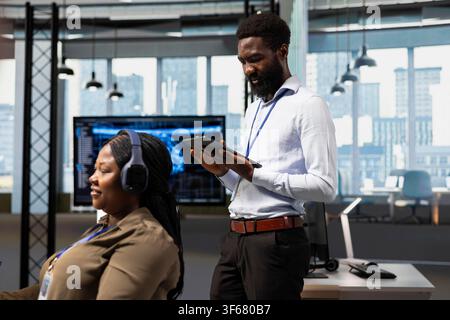 Technician developing applications using tablet, integrating AI next to office coworkers. IT specialist debugging applications with device using artificial intelligence in tech startup Stock Photo