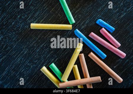 Creative educational design concept: Colored pencils and chalk for back to school with a black wooden chalkboard background Stock Photo