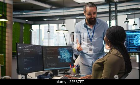 Pleased startup office manager applauding female programmer for optimizing code using AI. Satisfied team leader offering positive feedback to work done by IT specialist in office, camera A Stock Photo
