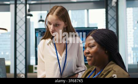 Smiling startup manager teaching junior dev how to use machine learning tech. Happy african american team leader showing intern in office how to use AI predictive models, camera A Stock Photo