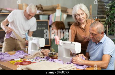 Some people communicate and discuss pattern, while others sew using sewing machine at lesson Stock Photo