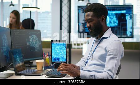 System administrator at office desk developing software using AI, listening music. IT expert wearing audio headset working on computer, debugging applications with artificial intelligence, camera A Stock Photo