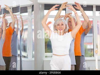 Active mature woman practicing fifth position holding by ballet barre together with others Stock Photo