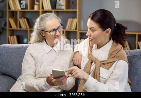 Senior woman with caregiver using smartphone at home, consultant guidance support Stock Photo