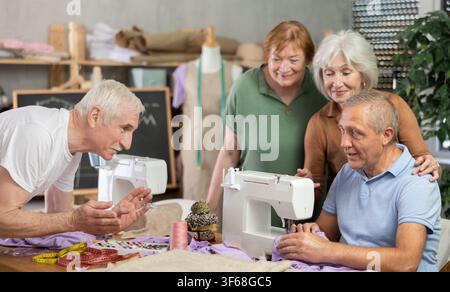 Male instructor demonstrating stitching at machine to older students Stock Photo