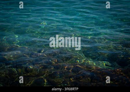 Crystal clear water surface texture with sun caustic reflections on the rocky sea floor Stock Photo