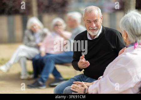 Elderly couple sitting on bench, flirting, chatting Stock Photo