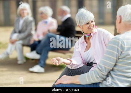 Elderly couple sitting on bench, flirting, chatting Stock Photo