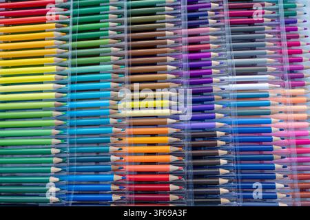 A wide angle and top-down view of a large professional set of colored pencils neatly organized in a transparent plastic case. The vibrant rainbow spec Stock Photo