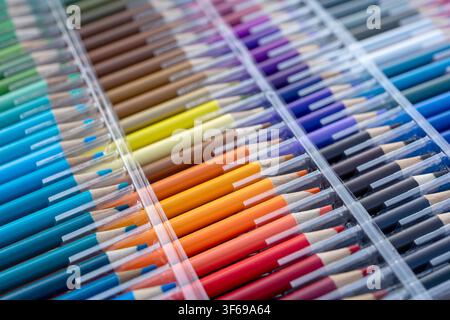 A wide angle and top-down view of a large professional set of colored pencils neatly organized in a transparent plastic case. The vibrant rainbow spec Stock Photo