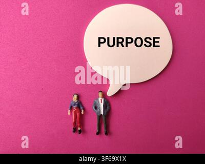 Miniature human figures stand beneath a speech bubble printed with the word PURPOSE on a pink background. Stock Photo