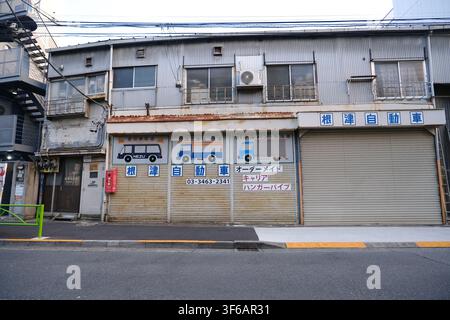 An old Japanese auto repair shop exterior with closed corrugated shutters, vehicle illustrations, and Japanese signage in Tokyo, Japan. Stock Photo