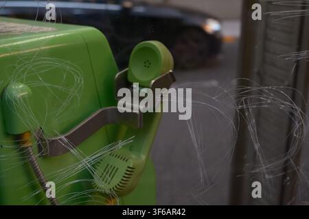 A close-up view of a green public payphone handset inside a telephone booth with scratched glass in Tokyo, Japan. Stock Photo