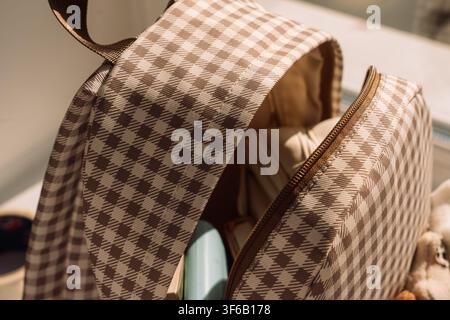 Open gingham backpack filled with school supplies in warm natural sunlight Stock Photo