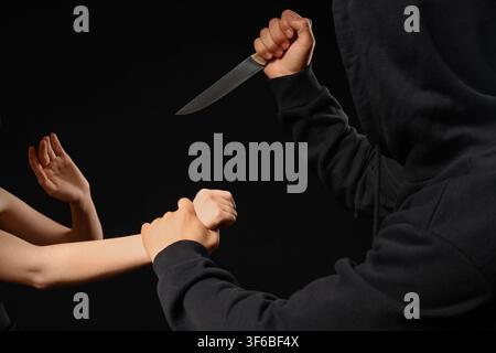 Hooded person holding a knife and grabbing a victims arm, crime and violence concept, self-defense and Danger Stock Photo