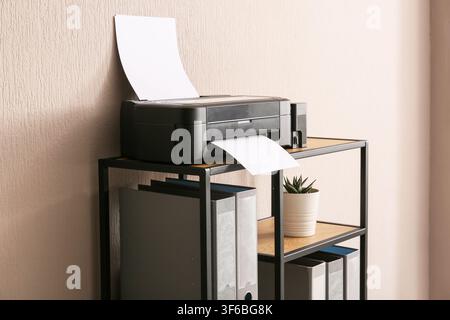 Modern black printer with paper on a wooden and metal shelf in a home office or workspace, the printer is actively printing a document, with paper fee Stock Photo