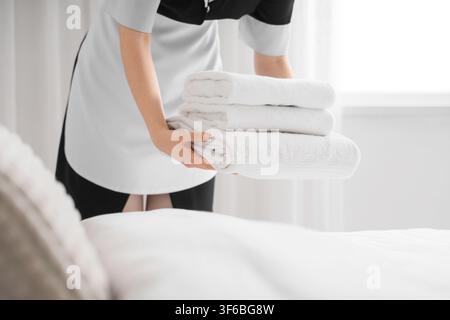 Hotel maid in uniform carrying a stack of clean white towels for room service and Hospitality, Hospitality and room service concept, emphasizing hygie Stock Photo
