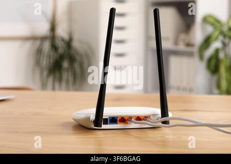 White wireless router with two antennas and connected ethernet cables on a wooden desk in an office setting, Several colorful ethernet cables are plug Stock Photo