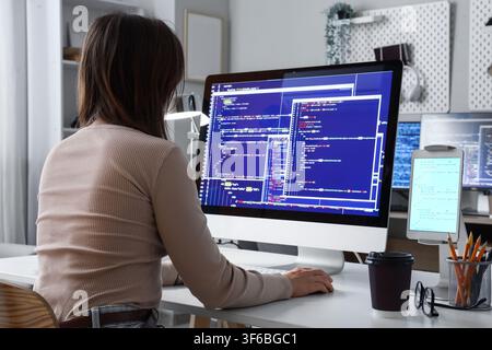 Female software developer coding on a desktop computer with multiple screens in a modern home office setting Stock Photo