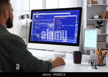 Male programmer coding on a desktop computer with multiple windows of script and data, software development Stock Photo