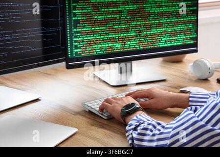 Programmer hands typing on keyboard with green code on multiple computer monitors, software development and cybersecurity Stock Photo