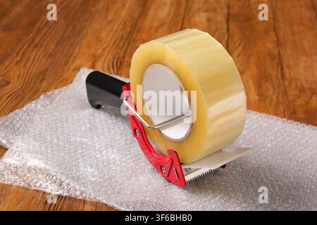 Clear packing tape dispenser with a roll of adhesive tape on bubble wrap, ready for shipping and moving Stock Photo