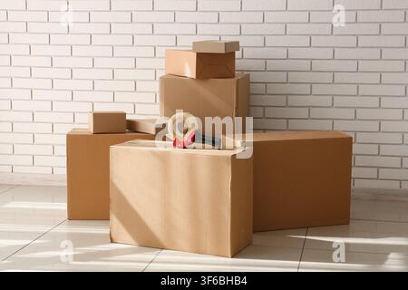 Stack of cardboard boxes with a tape dispenser on top, ready for moving or shipping against a white brick wall Stock Photo