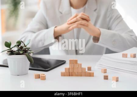 Businesswoman with clasped hands at a desk with Wooden blocks forming a growth chart and a stack of papers, Wooden blocks are arranged to form a risin Stock Photo