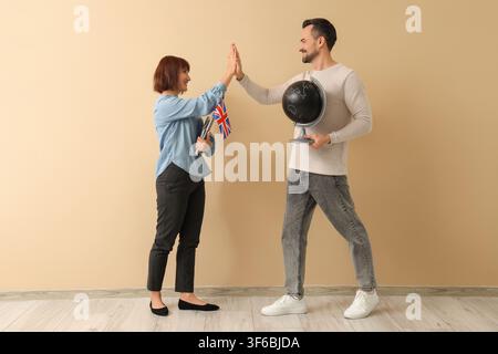 English and Geography teachers giving each other high-five near beige wall Stock Photo
