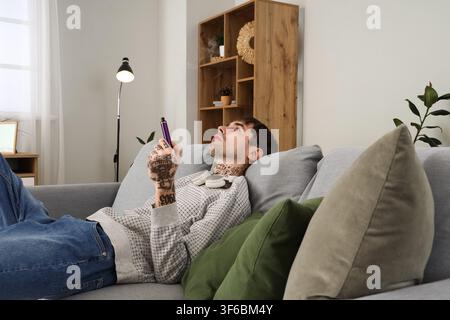Young man smoking disposable electronic cigarette and resting on sofa at home Stock Photo