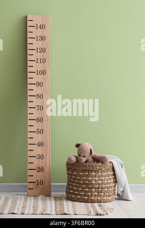 Basket with toy bear and stadiometer near green wall in room Stock Photo