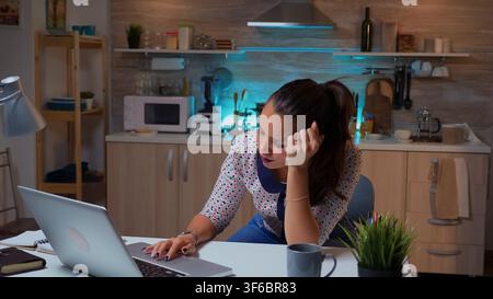 Woman closing eyes because of exhaustion while working on a project for work late at night. Busy exhausted remote employee napping on chair waking up reading on laptop using modern technology network Stock Photo