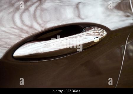 Close-up view of brown glossy metallic car door handle, featuring chrome proximity smart key sensor for intelligent keyless vehicle access and automat Stock Photo