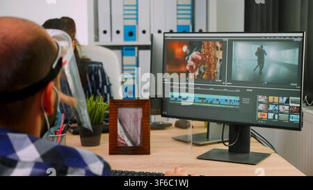 Wheelchair-using video editor wearing a mask discusses a creative production issue with a colleague while working in an office studio. Stock Photo