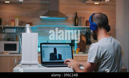 Man designer using cad software to design a 3D concept of buildings working overtime from home. Industrial male employee studying prototype idea on personal computer looking on device display Stock Photo
