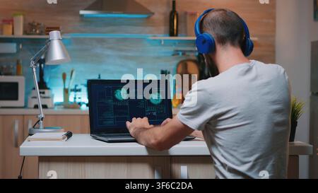 Back view of hacker with headset attacking succesfully the government using finetech, working from home in midnight. Programmer writing a dangerous malware for cyber attacks using performance device Stock Photo