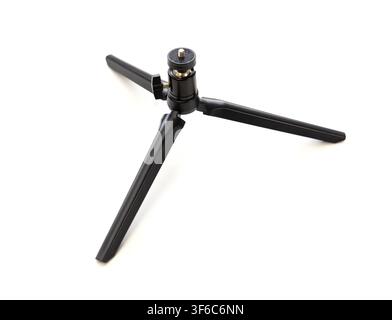 A small black camera tripod stands isolated against a clean white background Stock Photo