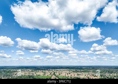 Drone aerial view of dramatic white cumulus clouds floating across a bright blue sky above tropical farmland and forest landscape during a sunny day. Stock Photo