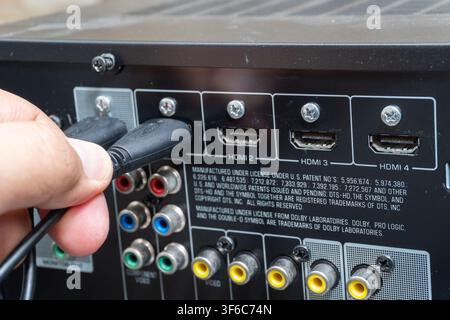Hand plugs HDMI cable into AV receiver. Close-up shows ports and connection details. Useful for tech, setup, or repair content Stock Photo