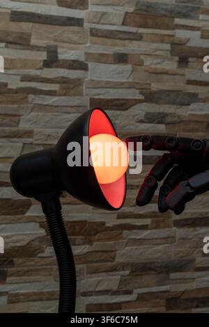 Black robotic or Prosthesis hand reaches toward a glowing yellow bulb in a modern desk lamp against a stone wall, useful for concepts of AI, innovatio Stock Photo