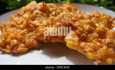 Extreme close-up shot capturing the glistening, crunchy texture and whole sweet corn kernels in traditional Indonesian bakwan jagung fritters. Stock Photo