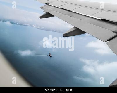 Aerial view of Tokyo from an airplane window, showing a ship sailing on the sea and clouds below during flight. Stock Photo