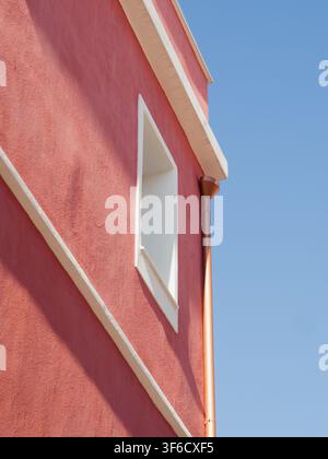 Pink plastered building facade with white window frame and copper drainpipe against clear blue sky. Stock Photo