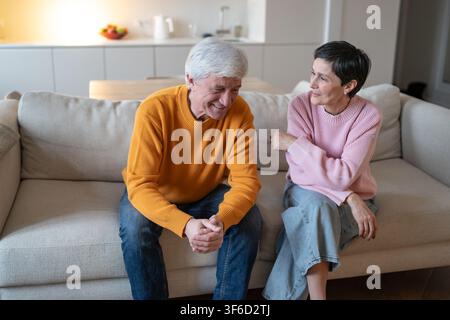Relaxed elderly couple husband and wife sitting on couch at home joking and having fun together. Stock Photo
