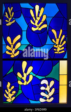 Abstract stained glass window designed by Henri Matisse, featuring stylized yellow and white botanical forms against deep blue geometric glass panels. Stock Photo
