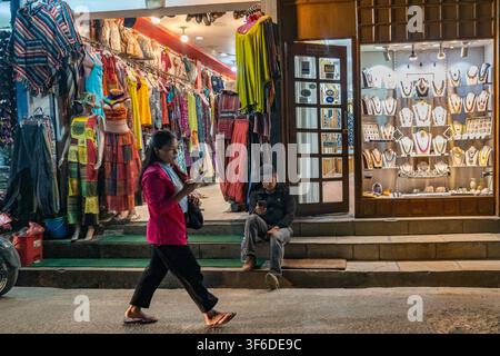 Kathmandu, Bagmati Province, Nepal - 04 April 2025: View of a woman walking past a clothing store and a man sitting on the steps in the Thamel distric Stock Photo